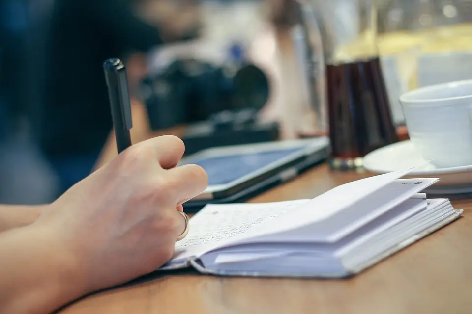 Persona revisando papeles y un cuaderno en el escritorio de un salón con luz natural